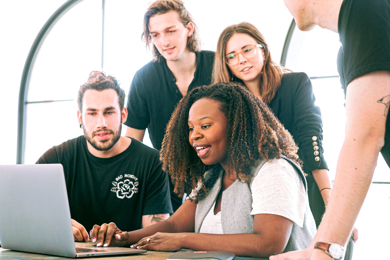 digital A diverse group of young professionals collaborating around a laptop in a modern office setting. Perfect for business or tech concepts.