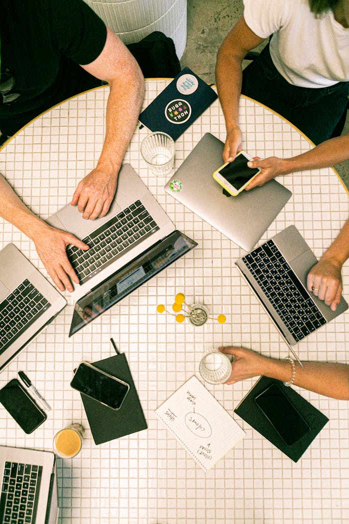 Services-03 Top view of a team collaborating with laptops, phones, and notes in a modern office.